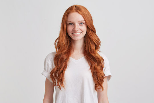 Portrait of cheerful beautiful young woman with long wavy red hair and freckles looks happy and smiling isolated over white background