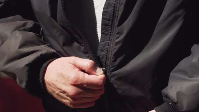 A white, middle aged man zips up his vintage hiking jacket slowly.