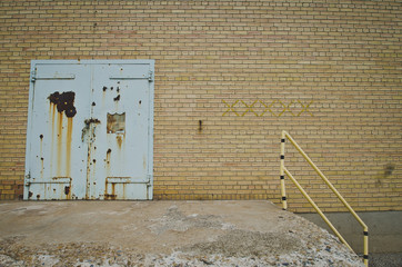 A rusty teal door on a yellow brick wall on a old closed building. 