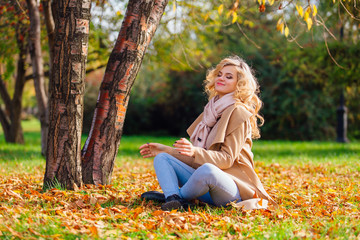 Young beautiful woman sitting on the ground coverd with fallen autumn leaves