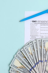 1041 tax form lies near hundred dollar bills and blue pen on a light blue background. US Income tax...