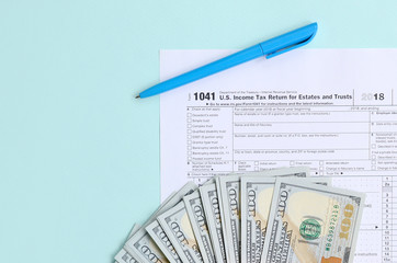 1041 tax form lies near hundred dollar bills and blue pen on a light blue background. US Income tax...