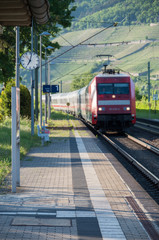 Obraz premium Red train entering train station with focus on platform clock