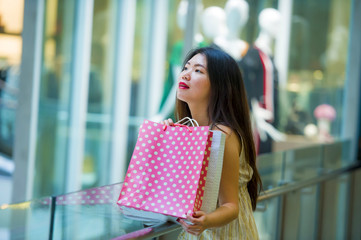 lifestyle indoors portrait of young happy and beautiful Asian Korean woman carrying shopping bags in mall buying cheerful walking around fashion store