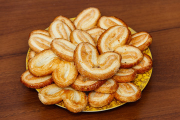 Palmier biscuits - french cookies made of puff pastry (also called palm leaves, elephant ears or french hearts) in a plate on wooden table