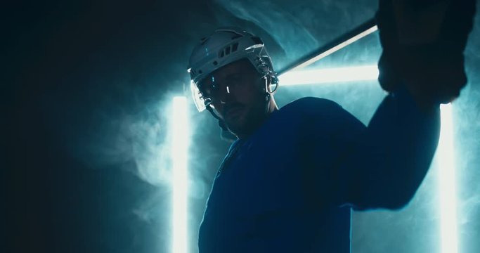 HANDHELD Portrait of Caucasian male ice hockey player in uniform, looking into the camera, dramatic lighting. 4K UHD 60 FPS SLOW MOTION