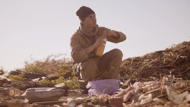 dirty homeless hungry man in a dump drinks the missing juice in the package with walking goes looking for food slow motion video. homeless dirty man roofless person looking for food in a dump. refugee