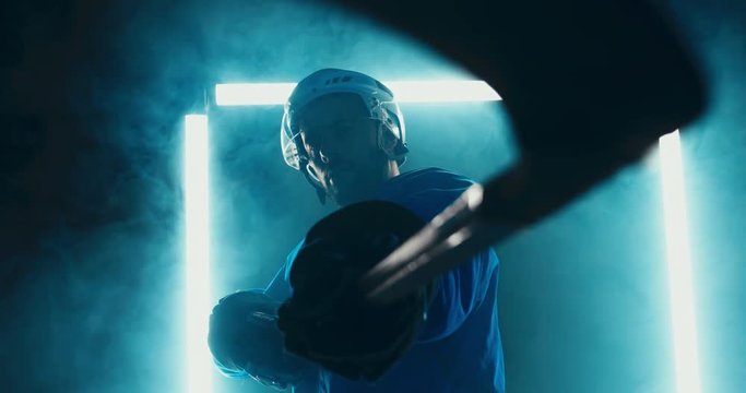 HANDHELD Portrait of Caucasian male ice hockey player in uniform, pointing stick into camera, dramatic lighting. 4K UHD 60 FPS SLOW MOTION