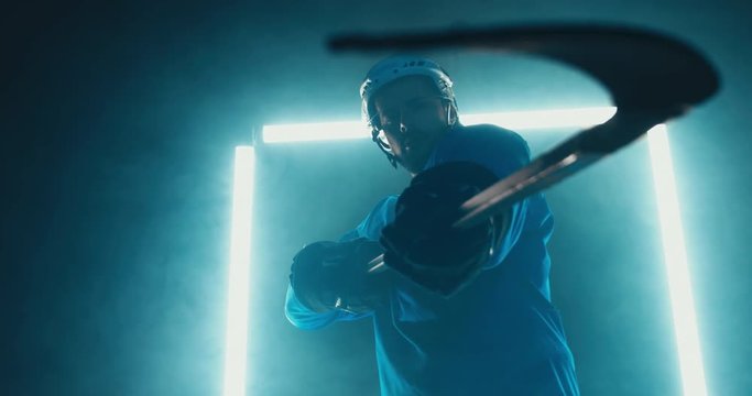 HANDHELD Portrait of Caucasian male ice hockey player in uniform, pointing stick into camera, dramatic lighting. 4K UHD 60 FPS SLOW MOTION