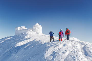 Three brave rescuers explore the terrain of snowy slope for avalanche danger against snow capped old observatory at peak of Carpathian mountain. Rear view. Winter seasonal landscape. Wanderlust series
