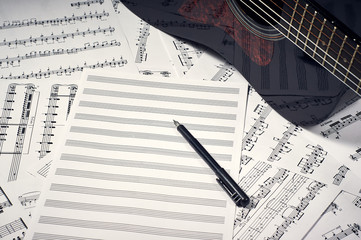 blank sheets for notes and pen on the background of sheets with notes and dark guitar, close-up