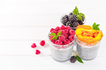 Food and drink, healthy eating and dieting concept. Homemade white chia pudding with fresh berries and green leaves for breakfast. Three glasses, raspberry, blackberry, apricot or peach.