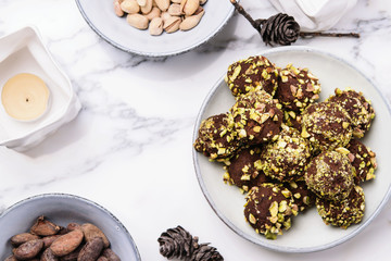 Homemade healthy vegan chocolate avocado truffles with pistachio in the bowl and ingredients, candle and fir cones on grey marble table. Organic energy vegetarian sweet balls. Hygge
