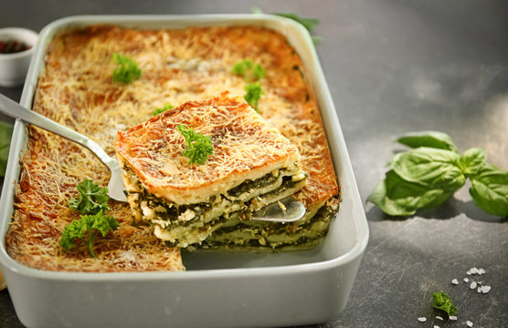 Spatula with piece of spinach lasagna over baking dish