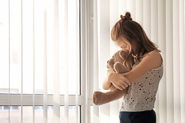 Little girl with teddy bear near window. Autism concept