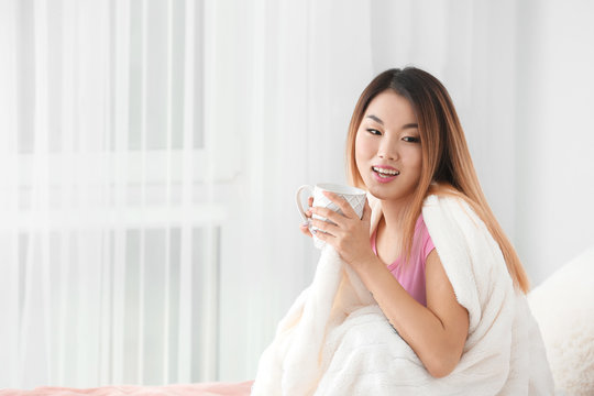 Beautiful smiling Asian woman with cup of tea at home