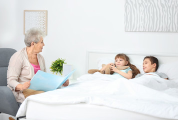 Obraz premium Senior nanny reading book to little children in bedroom