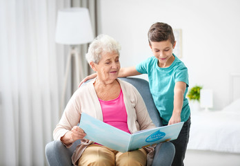 Senior nanny reading book to little boy indoors