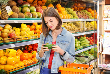 Beautiful woman choosing fresh avocado in supermarket