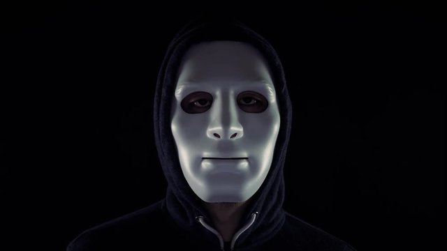 Video of a man in mask wearing a hoodie opening eyes and giving a creepy look at the looker in isolated dark background