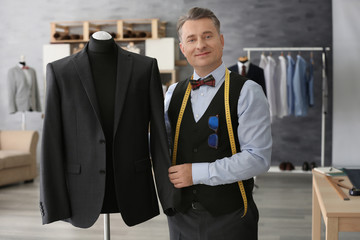 Tailor standing near mannequin with elegant jacket in atelier