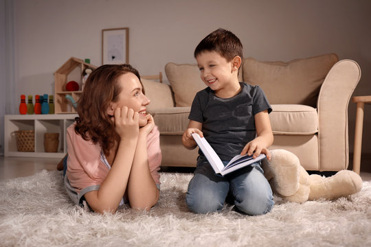 Cute little boy with his mother reading book at home in evening