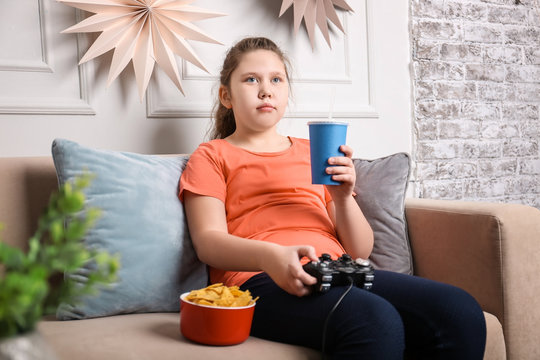 Overweight girl playing videogame with snacks indoors