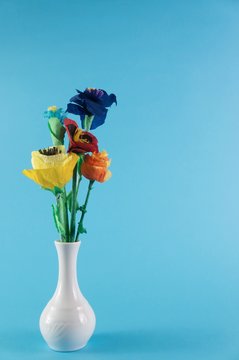 Origami flowers. Paper flowers. Handmade flowers in a ceramic vase on blue background.