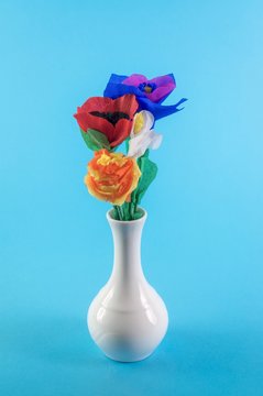 Origami flowers. Paper flowers. Handmade flowers in a ceramic vase on blue background.