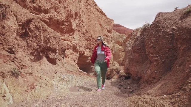 tourist is walking along the mountainous terrain. young woman traveler with backpack. red earth and mountains, like on Mars