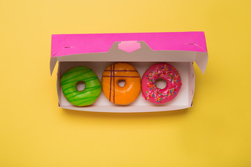 Color donuts in box on yellow background. Free space.