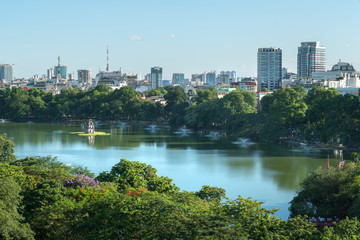 Obraz premium Hoan Kiem lake or Sword lake, Ho Guom in Hanoi, Vietnam with Turtle Tower, green trees and buildings on horizon