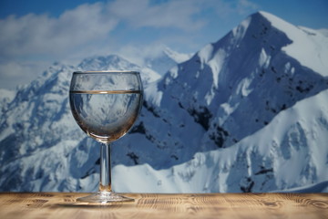 A glass of clean water stands on a wooden table against the winter mountain landscape.