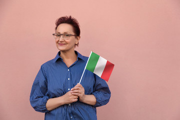 Italy  flag. Woman holding Italian flag. Nice portrait of middle aged lady 40 50 years old with a national flag over pink wall background outdoors. Learn Italian or visit Italy concept.