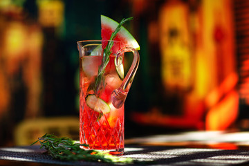 Closeup jug of watermelon sangria at colorful bar background.