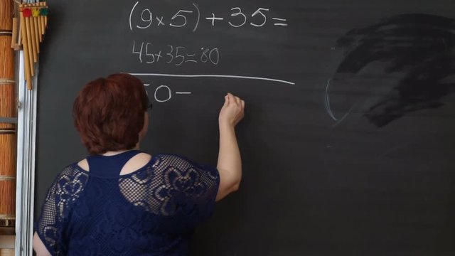 Teacher writing calculations on the blackboard in classroom
