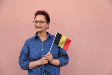 Belgium flag. Woman holding Belgian flag. Nice portrait of middle aged lady 40 50 years old with a national flag over pink wall background.