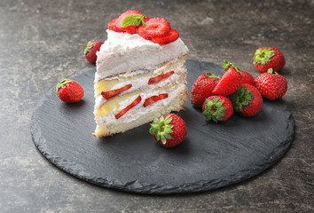 Slate plate with piece of delicious strawberry cake on table