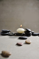 Obraz na płótnie Canvas White candle with pile of black stones on gray background