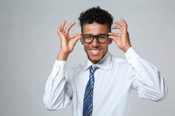 Handsome African-American businessman wearing glasses on grey background