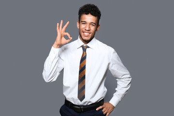 Handsome African-American businessman showing OK gesture on grey background