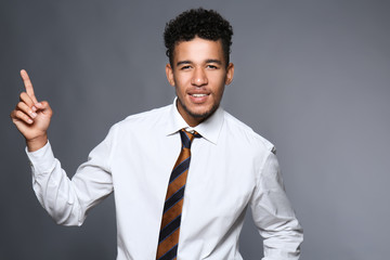 Handsome African-American businessman with raised index finger on grey background