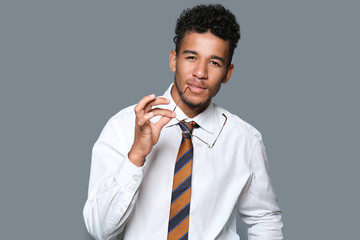 Handsome African-American businessman with glasses on grey background