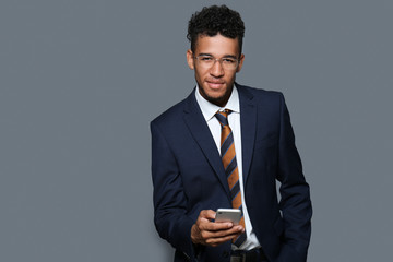 Handsome African-American businessman with mobile phone on grey background