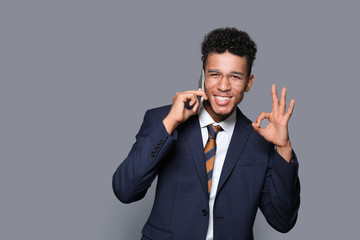 Handsome African-American businessman talking by mobile phone on grey background