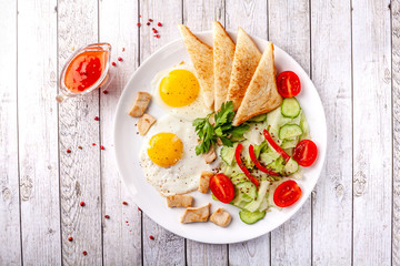 English cuisine, breakfast on a white plate of fried eggs, vegetables and salad with chicken, fried bread toast. Copy space, selective focus