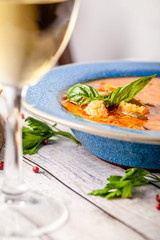 Italian European Cuisine. Spicy fish soup from seafood, salmon and trout, with vegetables in a blue plate. on the table in the restaurant is a glass of white wine. Copy space, selective focus