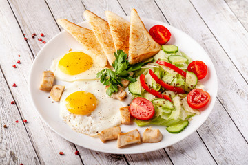 English cuisine, breakfast on a white plate of fried eggs, vegetables and salad with chicken, fried bread toast. Copy space, selective focus