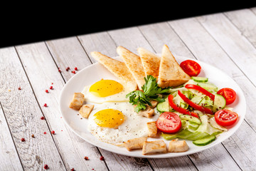 Fototapeta na wymiar English cuisine, breakfast on a white plate of fried eggs, vegetables and salad with chicken, fried bread toast. Copy space, selective focus