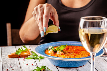 Italian Cuisine. The girl at the restaurant eats fish soup from seafood and salmon, squeezes lime into the soup and drinks white wine. Copy space, selective focus